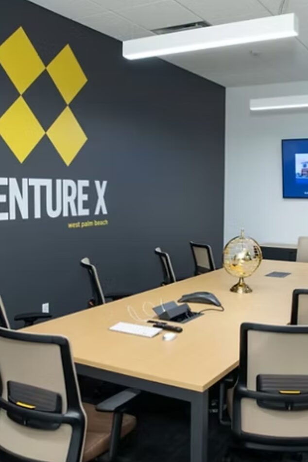 Modern conference room with 'Venture X' logo on the wall, chairs around a table with a phone and notepads.