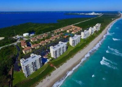 Aerial view of coastal apartments alongside a turquoise ocean with a backdrop of greenery.